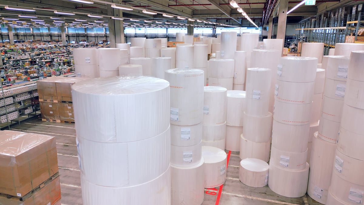 A vast warehouse reveals massive stacks of white rolls